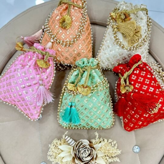 handmade embroidered potli bags in pink, peach, mint green, ivory, and red colors with pearl detailing, golden tassels, and drawstring closure for wedding favors and festive gifting.